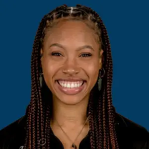 Smiling woman with braided hair against a blue background, wearing a black top.